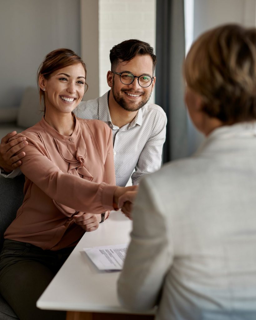 Happy couple greeting their real estate agent in the office. Young happy couple shaking hands with insurance agent during a meeting in the office.